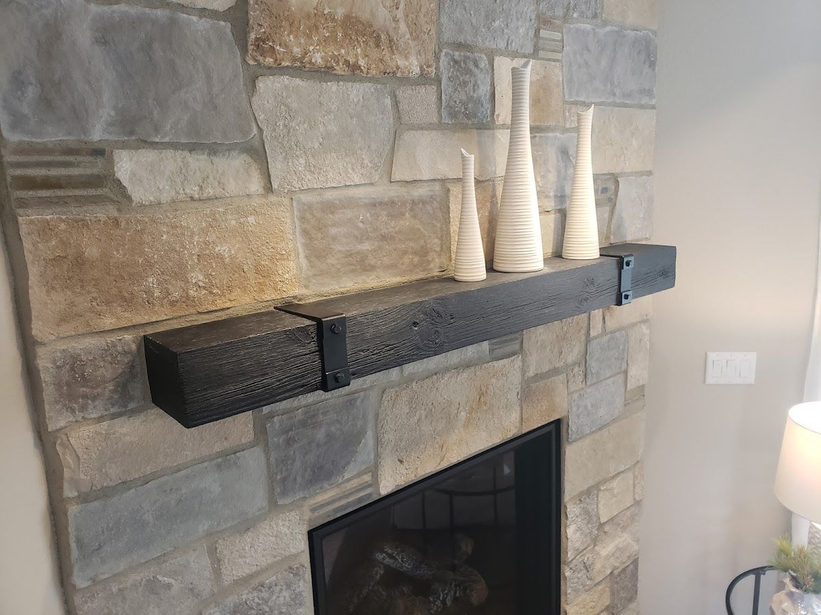 Stone fireplace with black mantel, three white decorative vases.