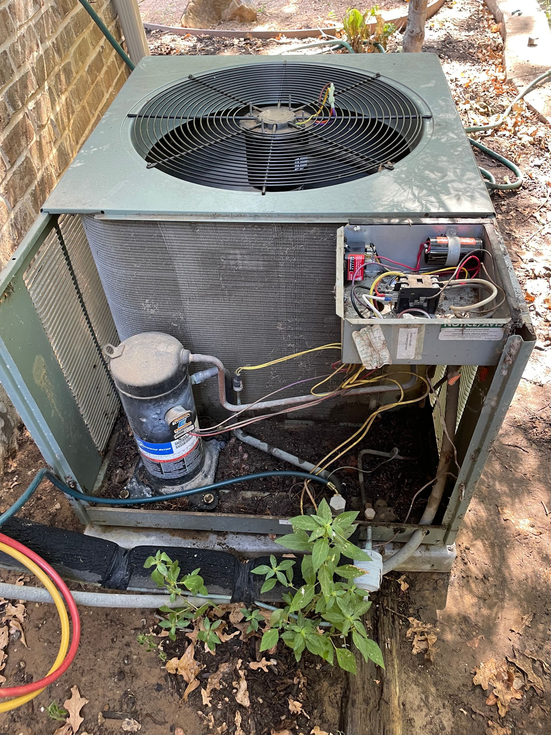 Air conditioning service repair. A metal outdoor air conditioning unit with its side panel removed, exposing the compressor and electrical components.