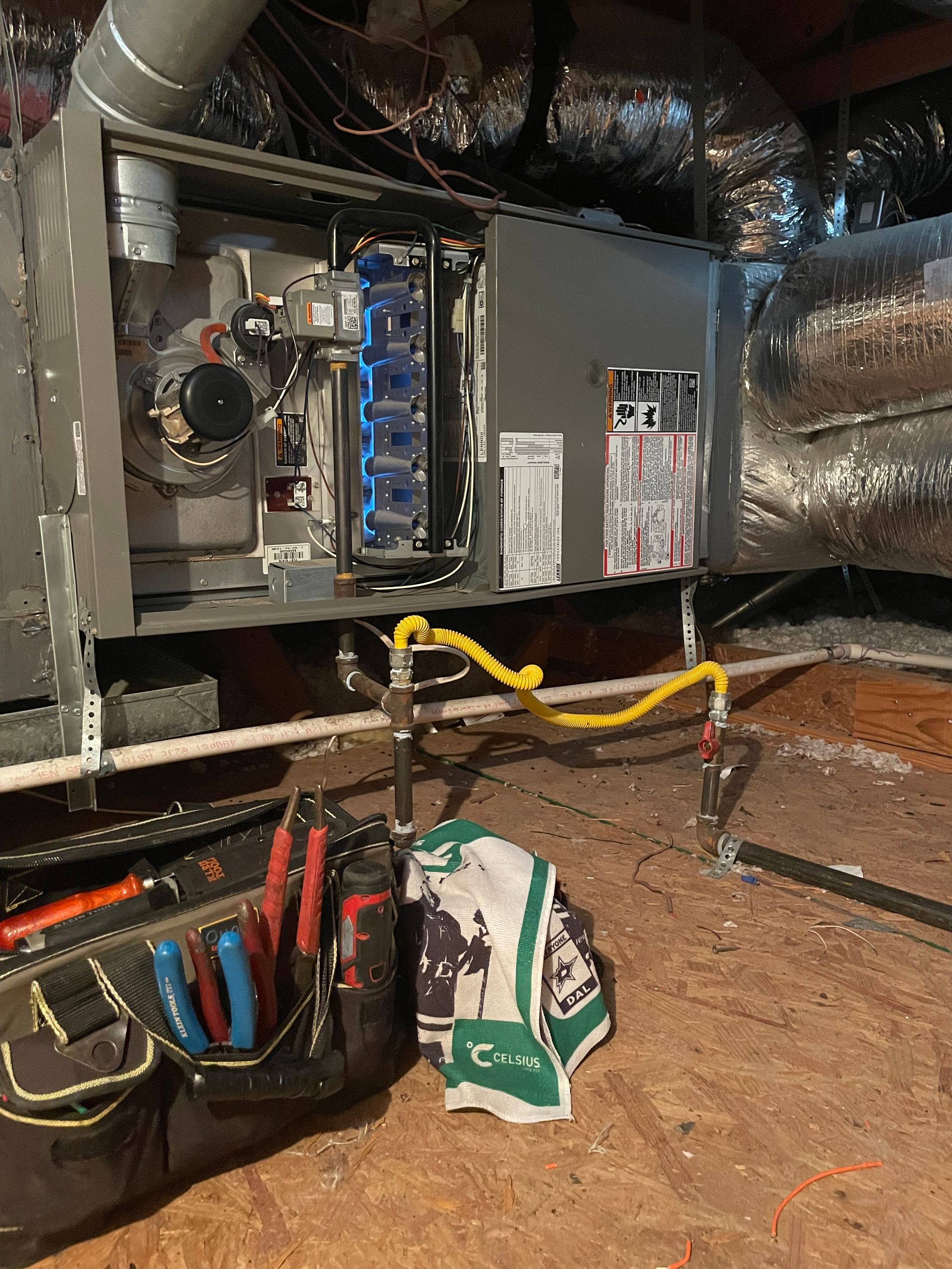 HVAC furnace repair - A furnace unit in an attic with its maintenance panel open, showing internal components, wiring, and a yellow gas line.