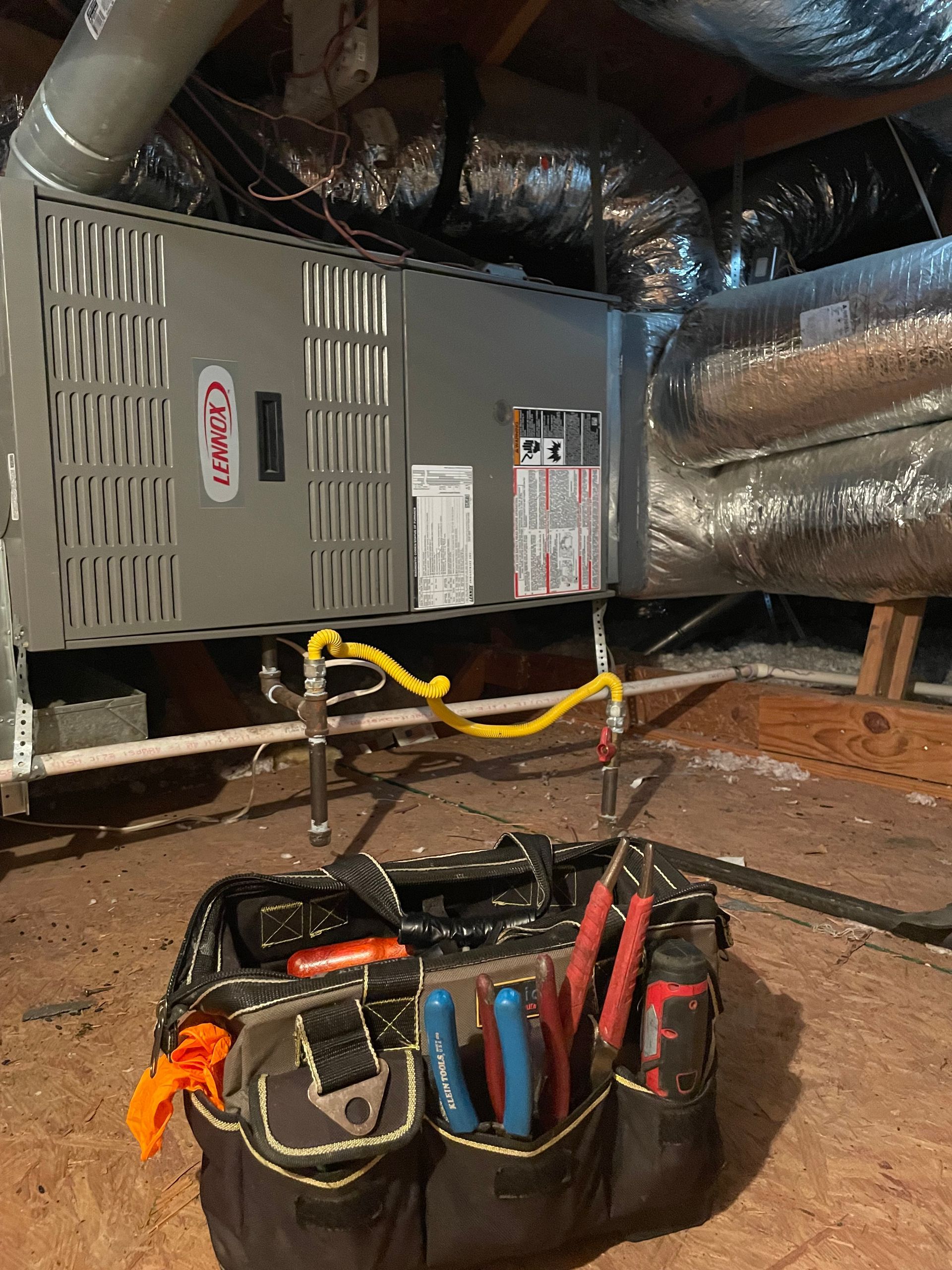 HVAC Repair  job - A tool bag sits on the floor of an attic in front of a Carrier brand HVAC furnace unit with attached ductwork.
