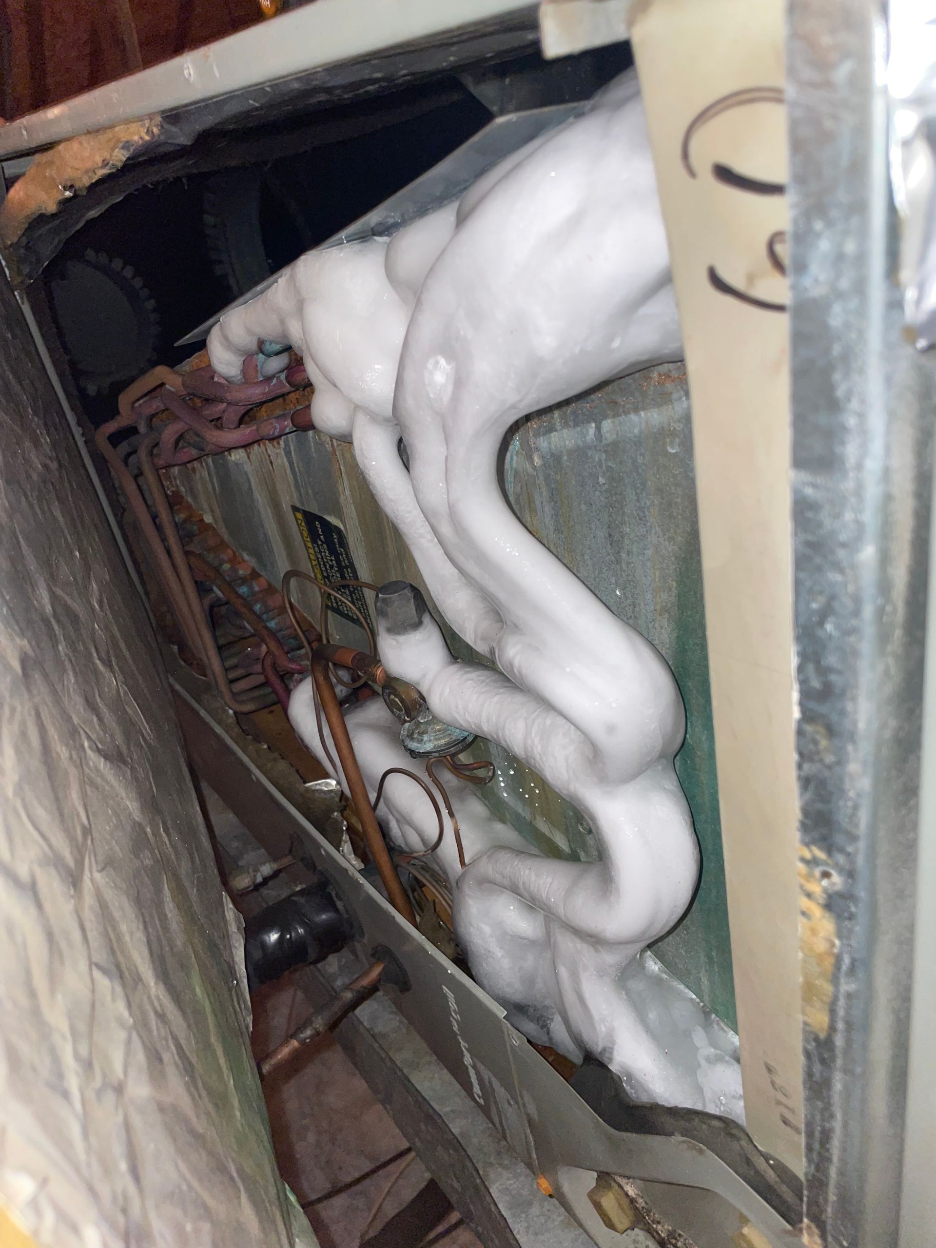 A close-up view of an indoor air conditioning evaporator coil heavily coated in thick, white ice buildup.