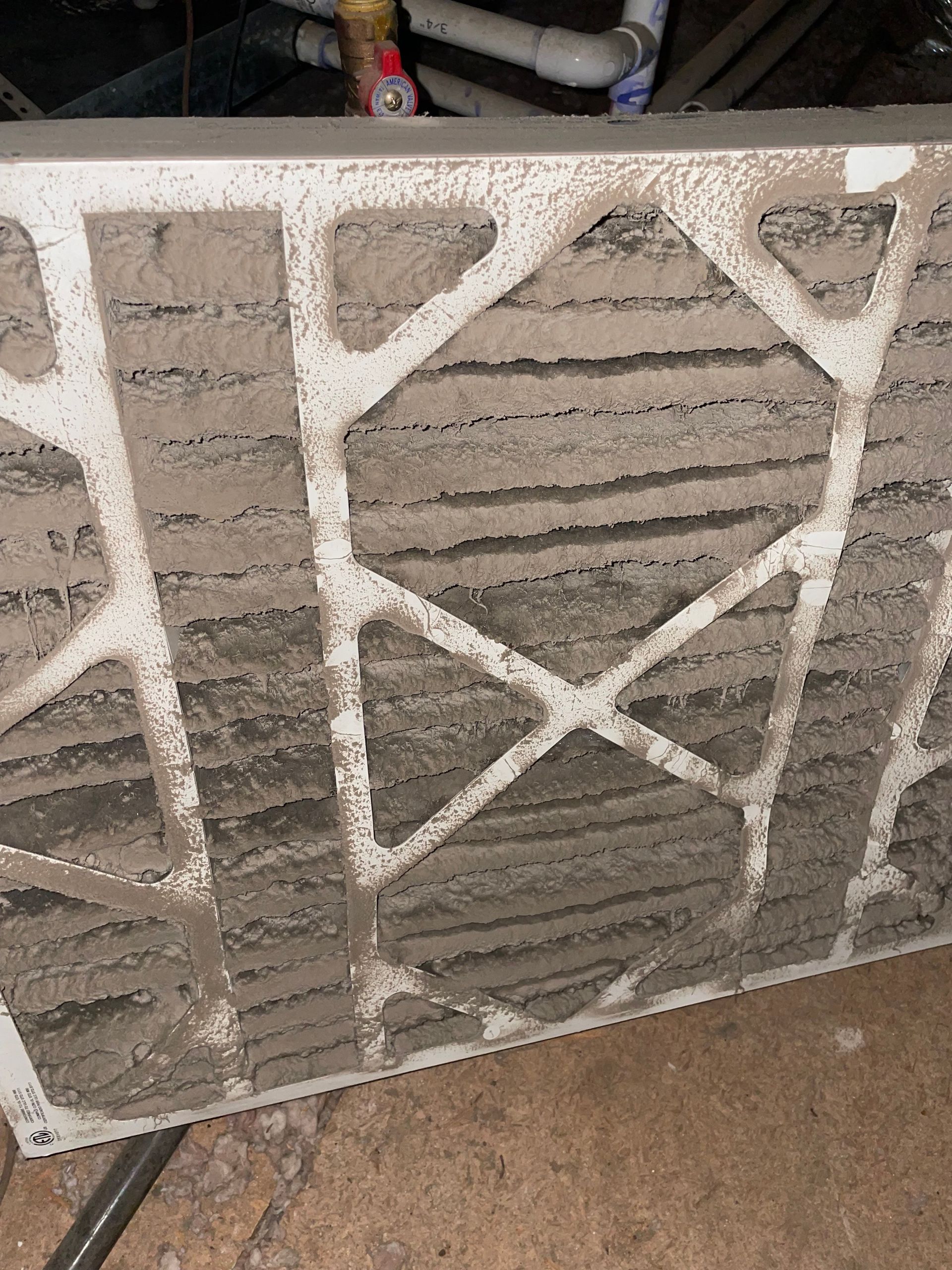 HVAC Maintenance - A heavily dust-covered HVAC air filter with a white cardboard frame, showing thick, gray debris trapped in its pleats.