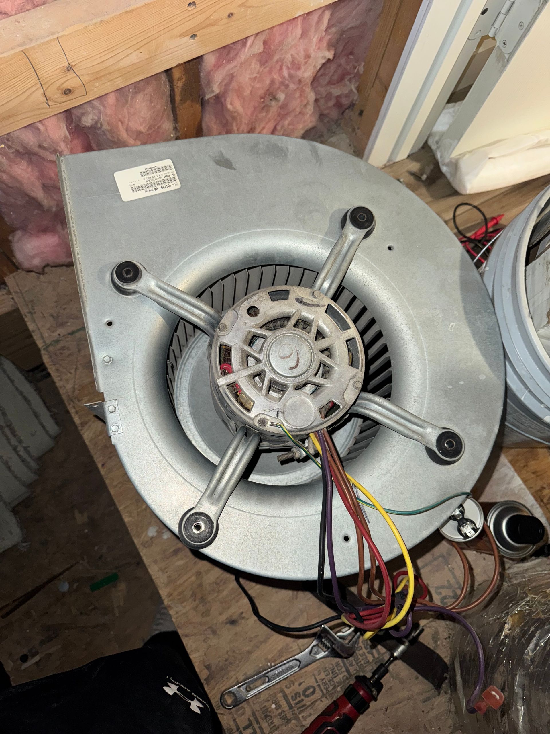 HVAC Repair job. A metallic blower motor unit with wires, mounted on a metal housing, resting on a wooden surface in a utility area.