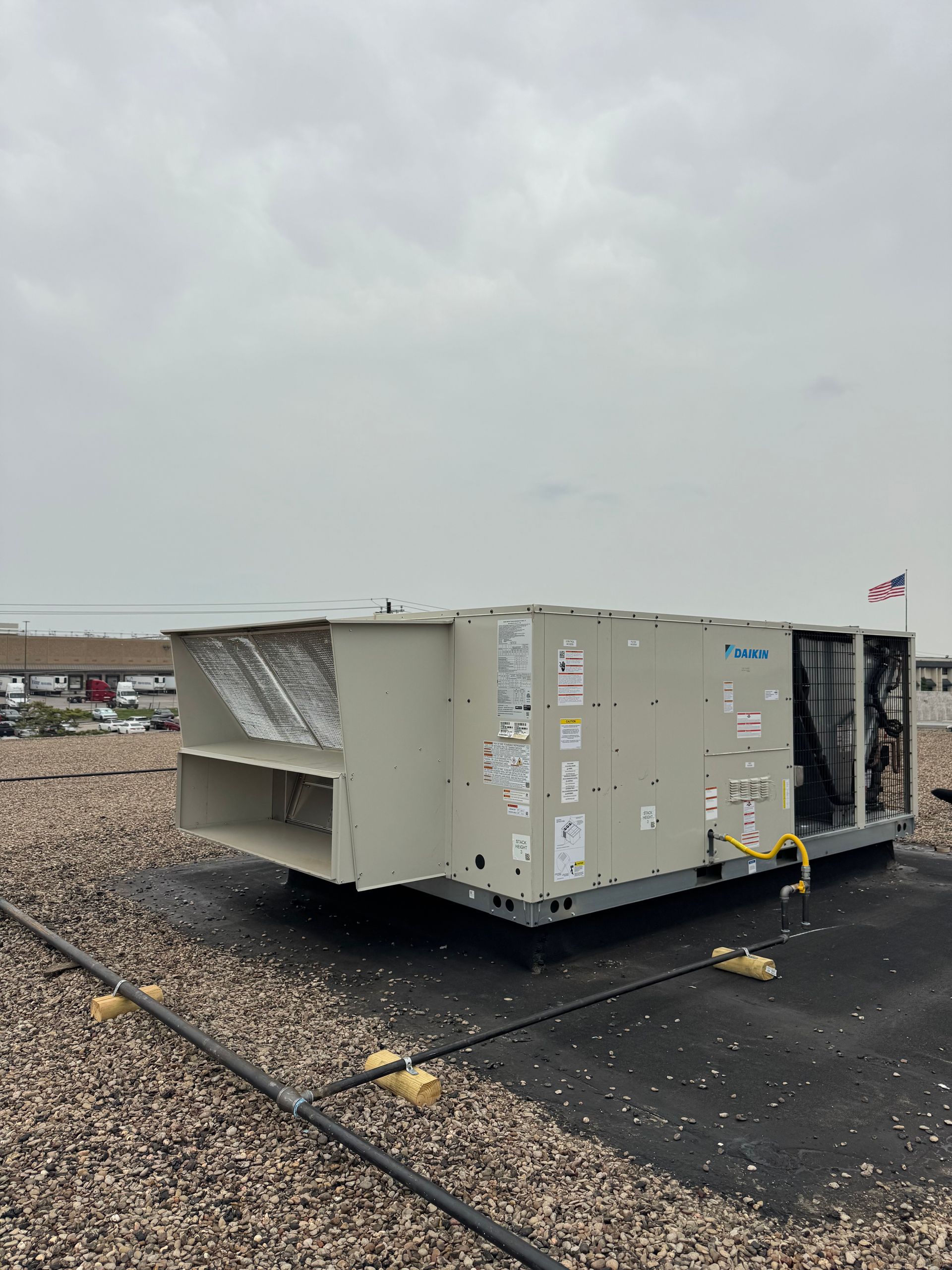 Commercial HVAC job. A beige commercial rooftop HVAC unit sits on a flat roof covered in gravel under a cloudy sky.