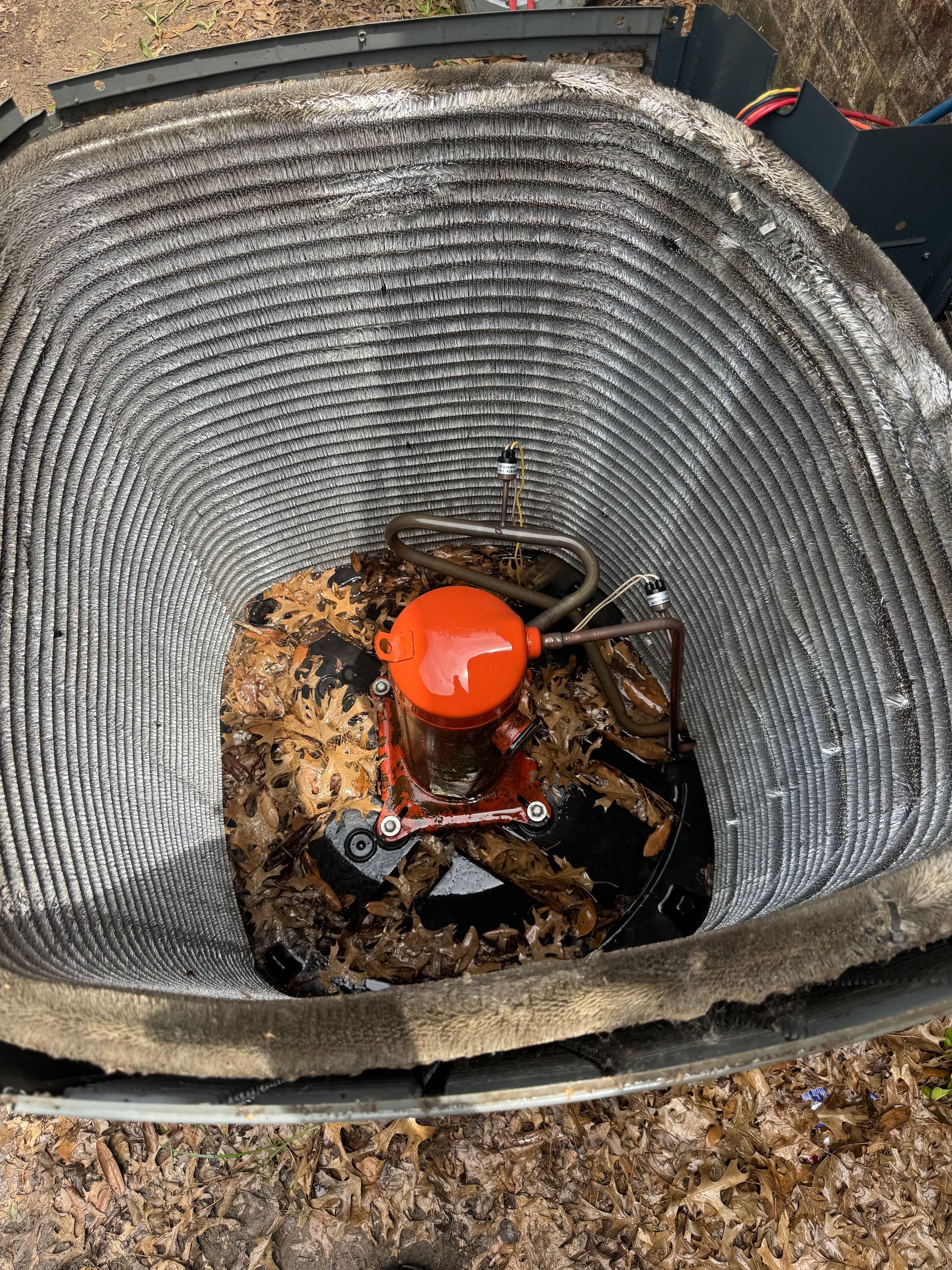 HVAC Service job . Top-down view of an outdoor HVAC unit interior, showing a round orange motor covered in accumulated dead leaves and debris.