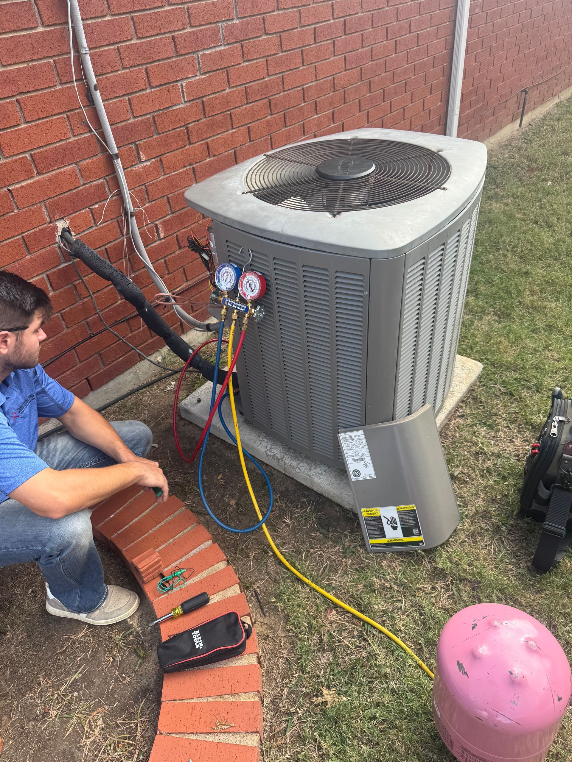 A Serv Tech Pro technician in a blue shirt services an outdoor air conditioning unit connected to pressure gauges and a refrigerant tank.