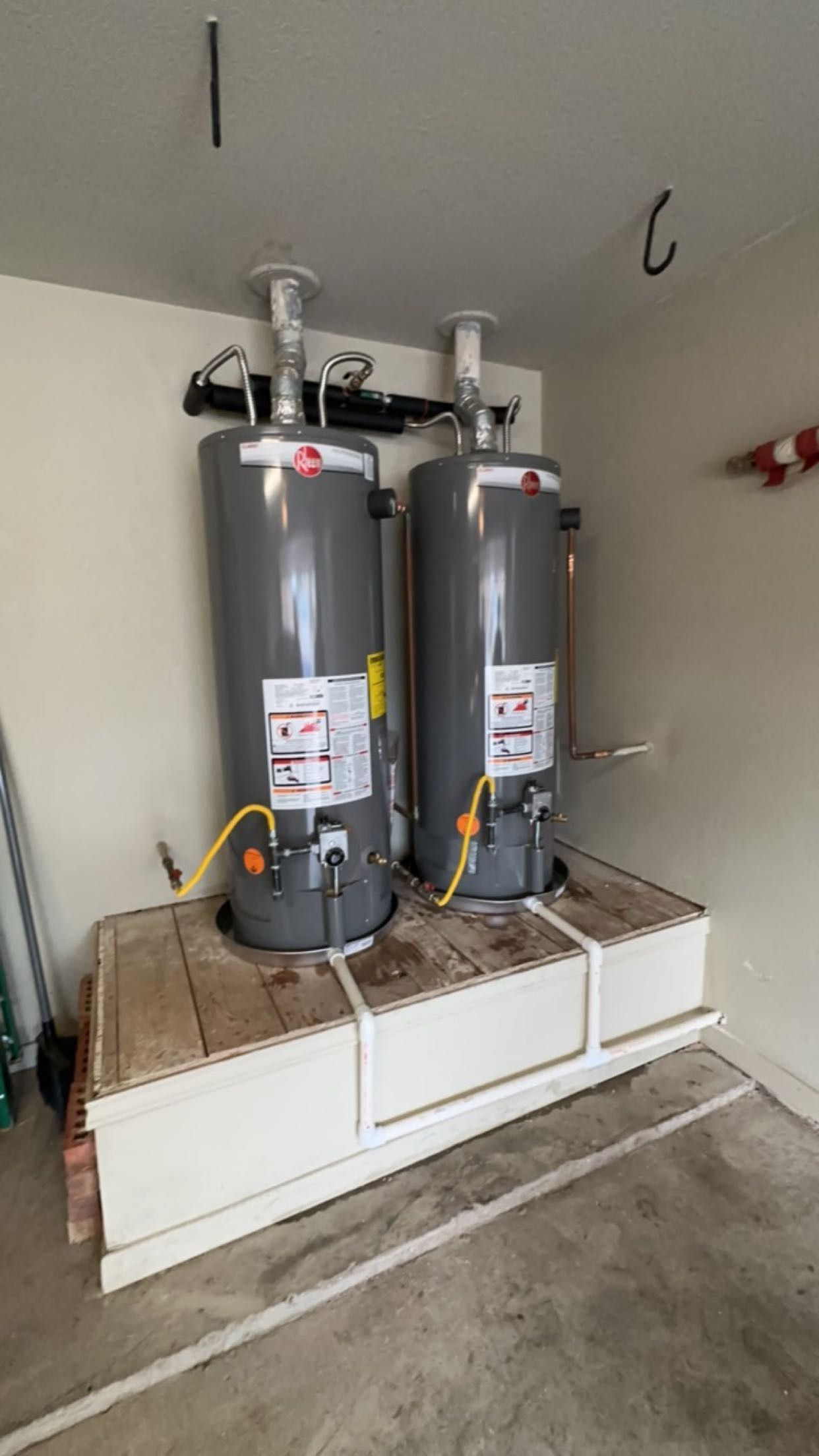 Two gray gas water heaters installed side-by-side on a white wooden platform in a residential garage.