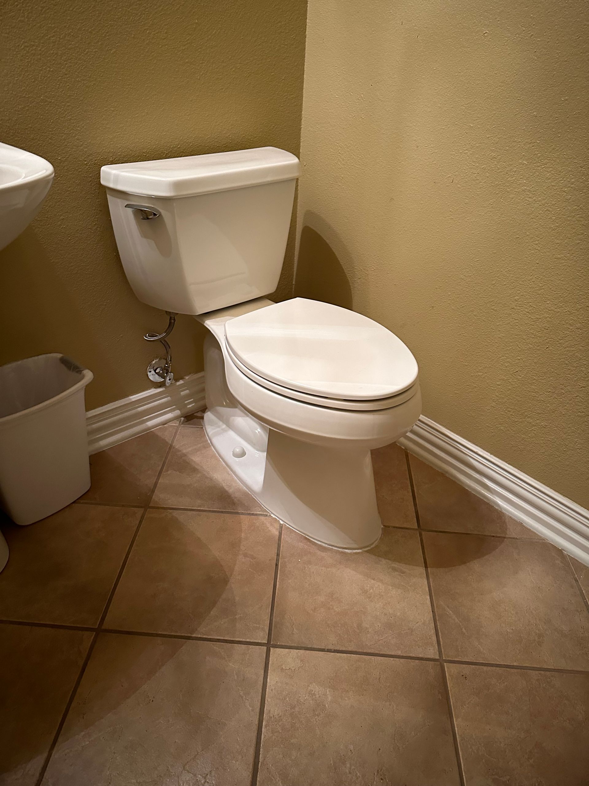 Plumbing job - new toilet install . A white porcelain toilet with a closed lid, situated in a bathroom with beige textured walls and tiled flooring.