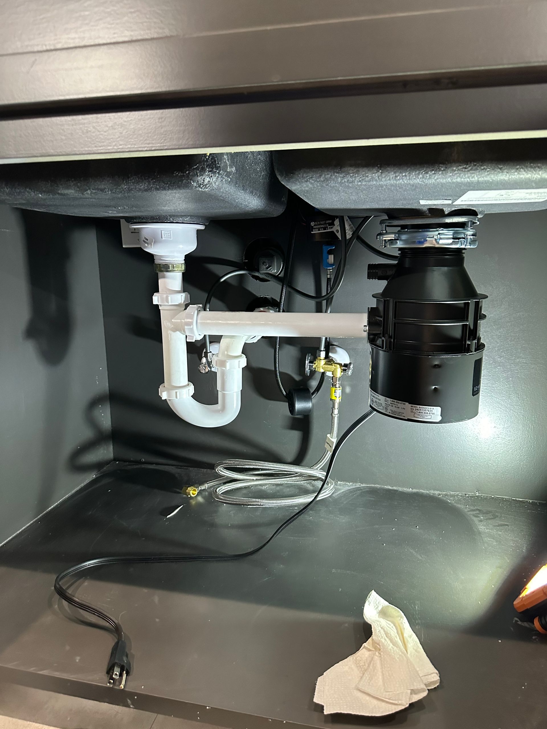 Plumbing work. A black garbage disposal and white PVC piping installed under a kitchen sink.