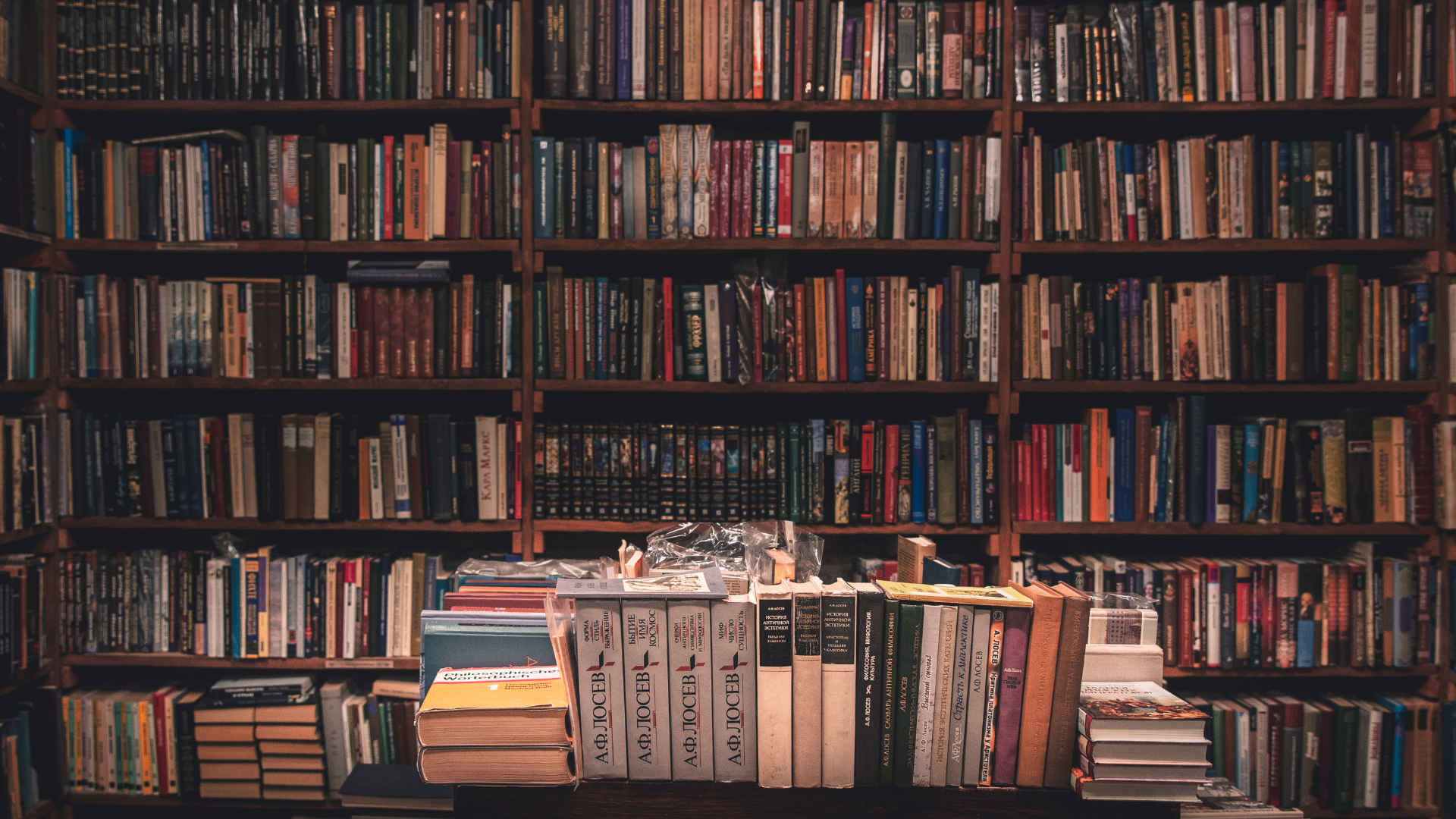 Bookshelves packed with books behind a table stacked with assorted books and magazines