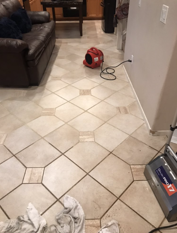 Living room with tiled floor, brown sofa, red vacuum cleaner, and a cord along the wall.