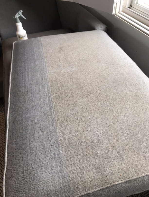 Gray upholstered ottoman beside a window, with a spray bottle on the armrest