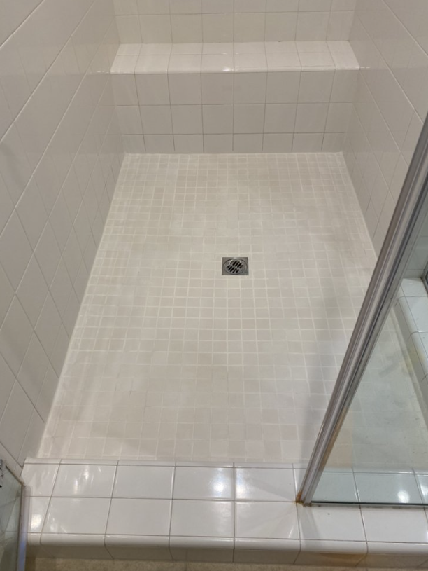 Empty tiled shower with a square drain and glass door panel, viewed from above.