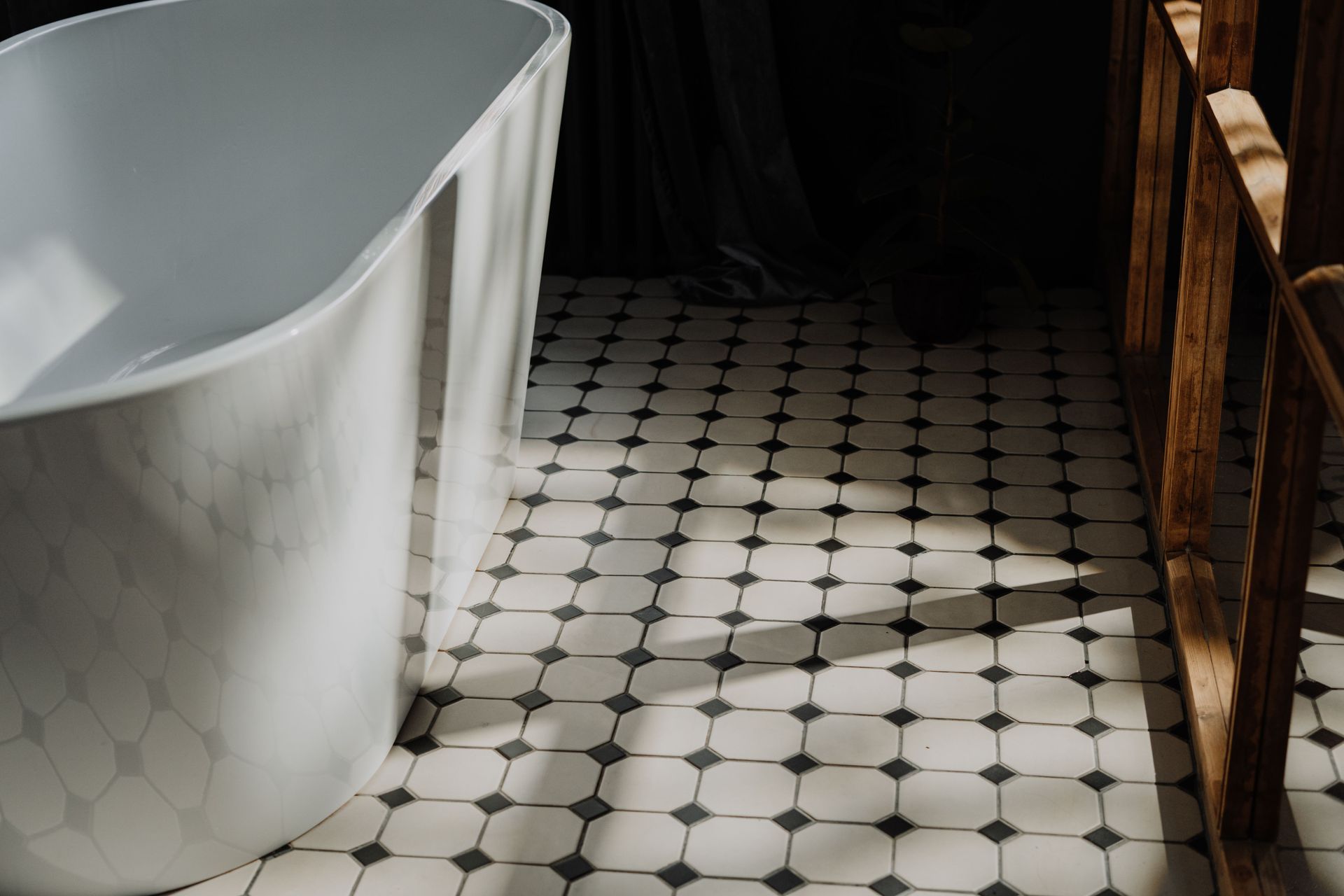 White clawfoot bathtub beside a black-and-white tiled floor in a dim bathroom.