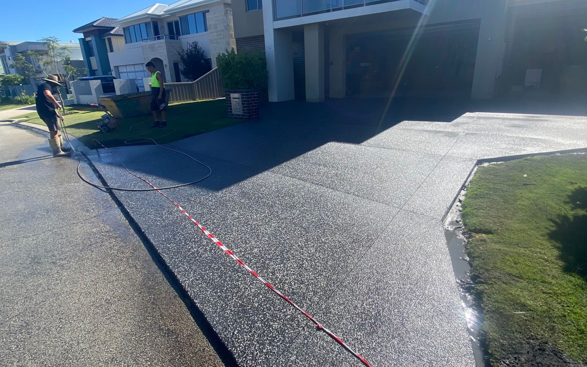 Newly poured charcoal exposed aggregate driveway beside a house, with red tape marking the line across the pavement.