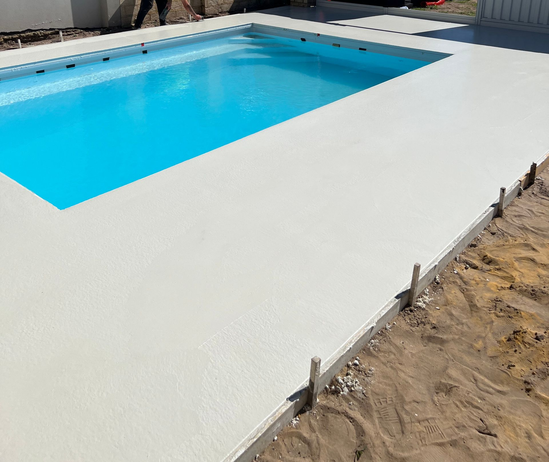 Close up of decorative exposed aggregate concrete pool edging around rectangle blue pool.