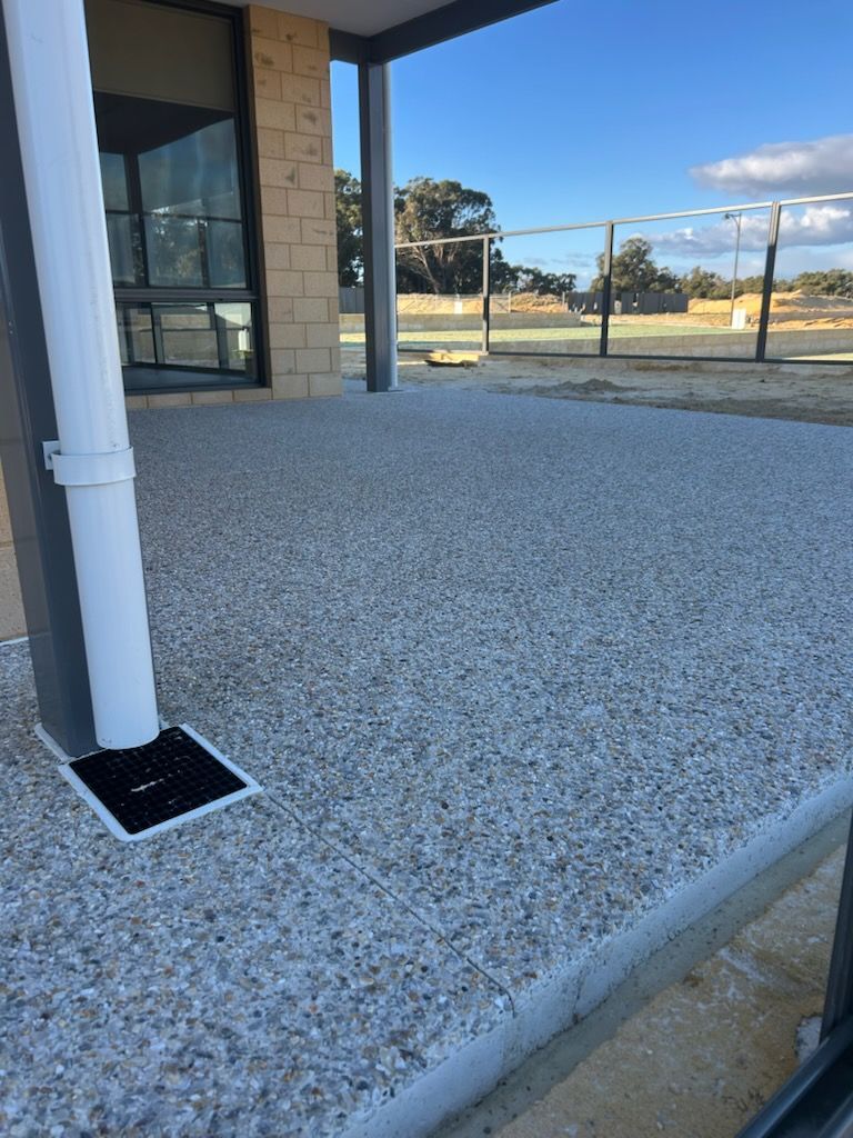 Covered patio with white gravel flooring, a support column, and a view of the yard through glass doors.