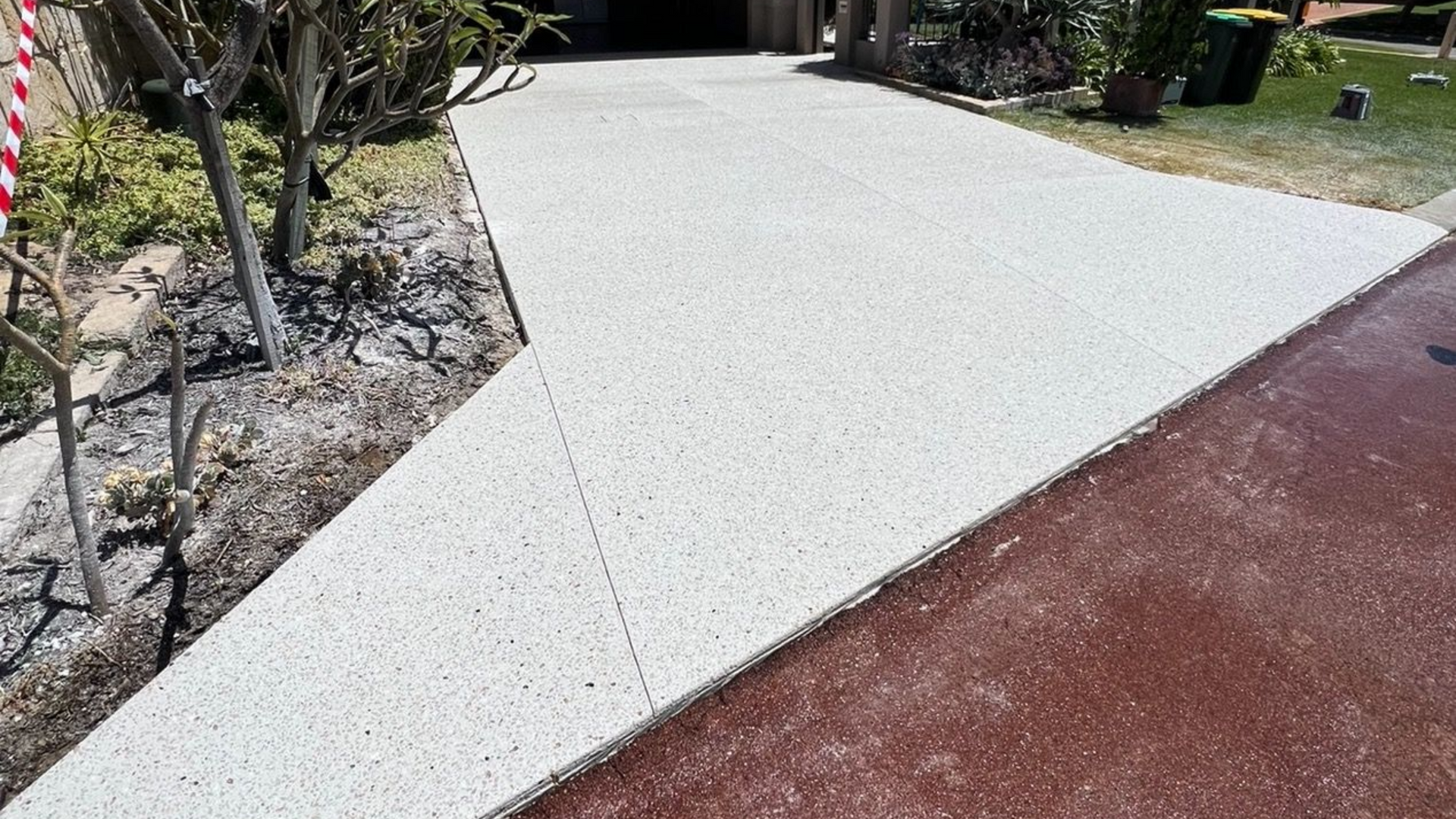 Curved white concrete walkway beside a red paved path and landscaped garden bed.