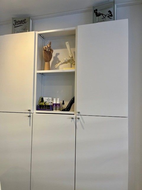 Witte keukenkastjes met een open plank in het midden waarop flessen, decoratie en hangend keukengerei staan.