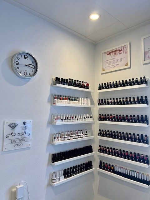 Aan de muur bevestigde planken met kleine flesjes in een witte ruimte, zoals in een schoonheidssalon of nagelstudio.