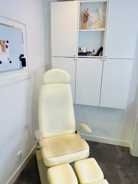 Gevoerde relaxstoel in een lichte behandelkamer met witte kasten en een donkere vloer.