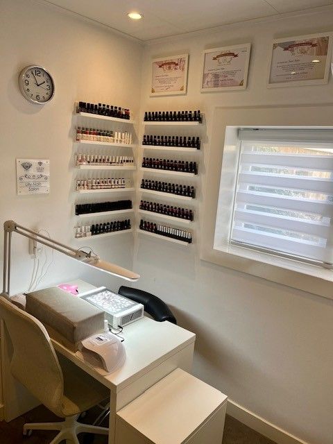Nagelsalonhoek met manicuretafel, flesjes nagellak op wandplanken en een raamjaloezie.