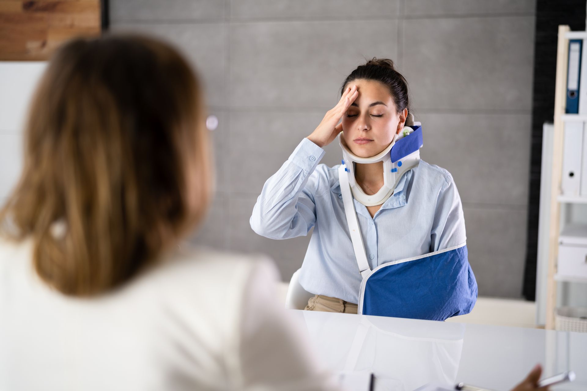 Woman in a blue sling rubbing her forehead in a bathroom mirror, looking stressed.