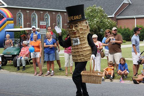 Man dressing in peanut costume walking in a parade with a crowd behind him