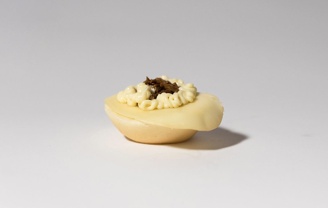 Antipasto: pasta sfoglia bianca a forma di conchiglia, ripiena di crema e guarnita con una glassa scura sbriciolata.