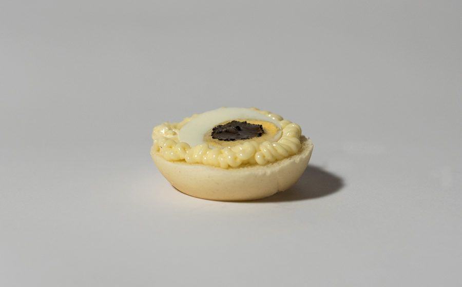 Antipasto di uova alla diavola con ripieno giallo, uovo bianco e centro scuro, su sfondo bianco.