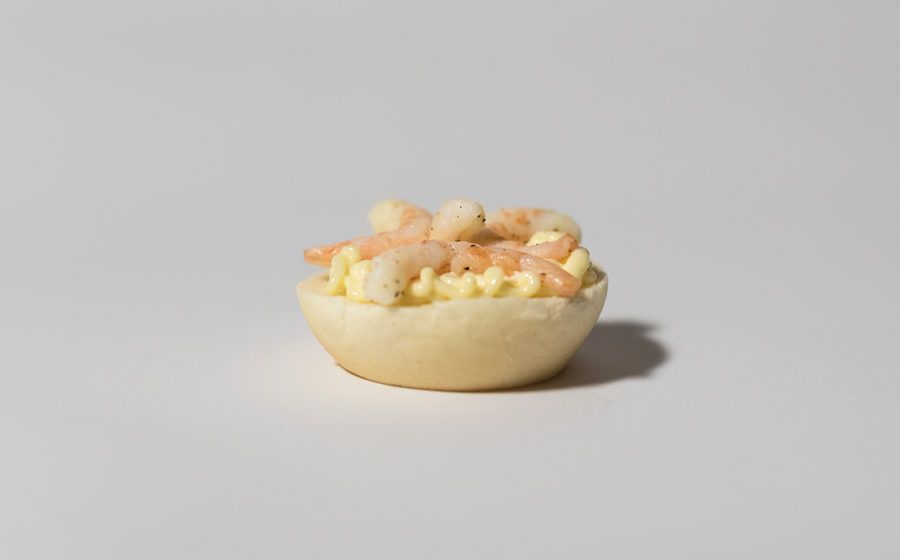 Antipasto di gamberi in un guscio di pasta sfoglia, ripieno di crema gialla, su fondo bianco.