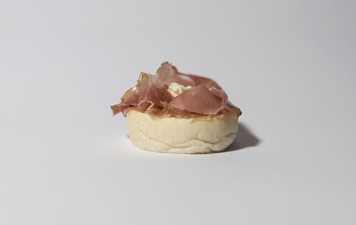 Primo piano di un piccolo panino ricoperto di carne e di una crema spalmabile.