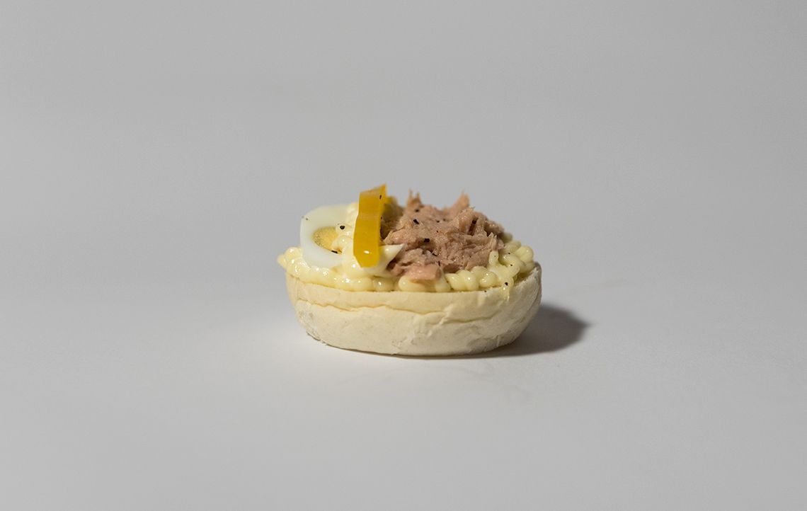 Antipasto di insalata di tonno su una base di pane bianco, con una fetta di peperone giallo e una fetta di uovo.