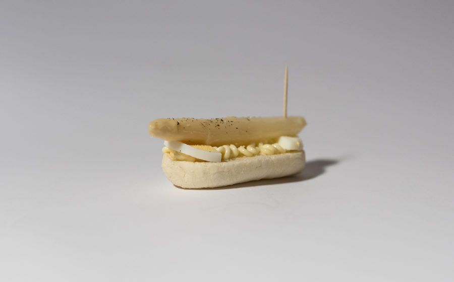 Mini panino ripieno, tenuto insieme da uno stuzzicadenti e appoggiato su una superficie bianca.