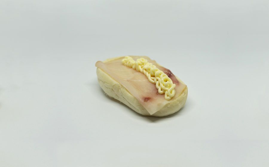 Piccolo sushi con una fetta di carne ricoperta di salsa gialla su sfondo bianco.