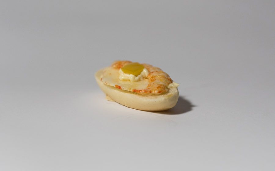 Piccolo antipasto a forma di barchetta con ripieno cremoso e guarnizione gialla, su una superficie bianca.