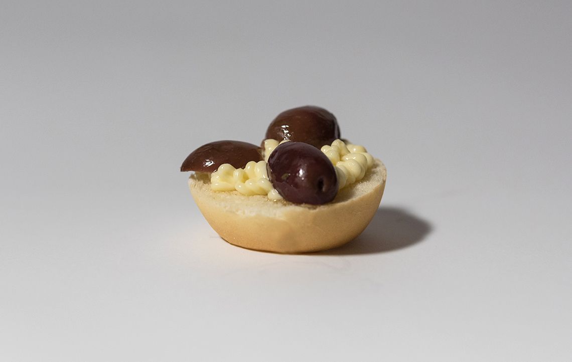 Un boccone di pane con una crema spalmabile gialla e tre olive scure.