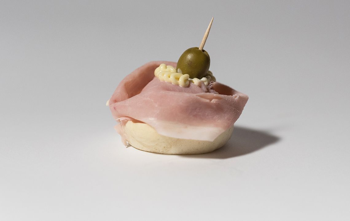 Antipasto: fetta di prosciutto su pane condita con crema spalmabile e un'oliva infilzata su uno stuzzicadenti.