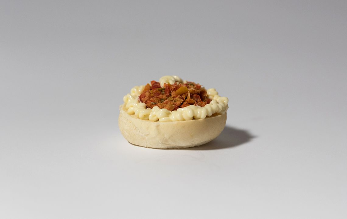 Piccola crostata con crosta chiara, bordo cremoso e centro farcito con una copertura rosso-marrone su una superficie bianca.