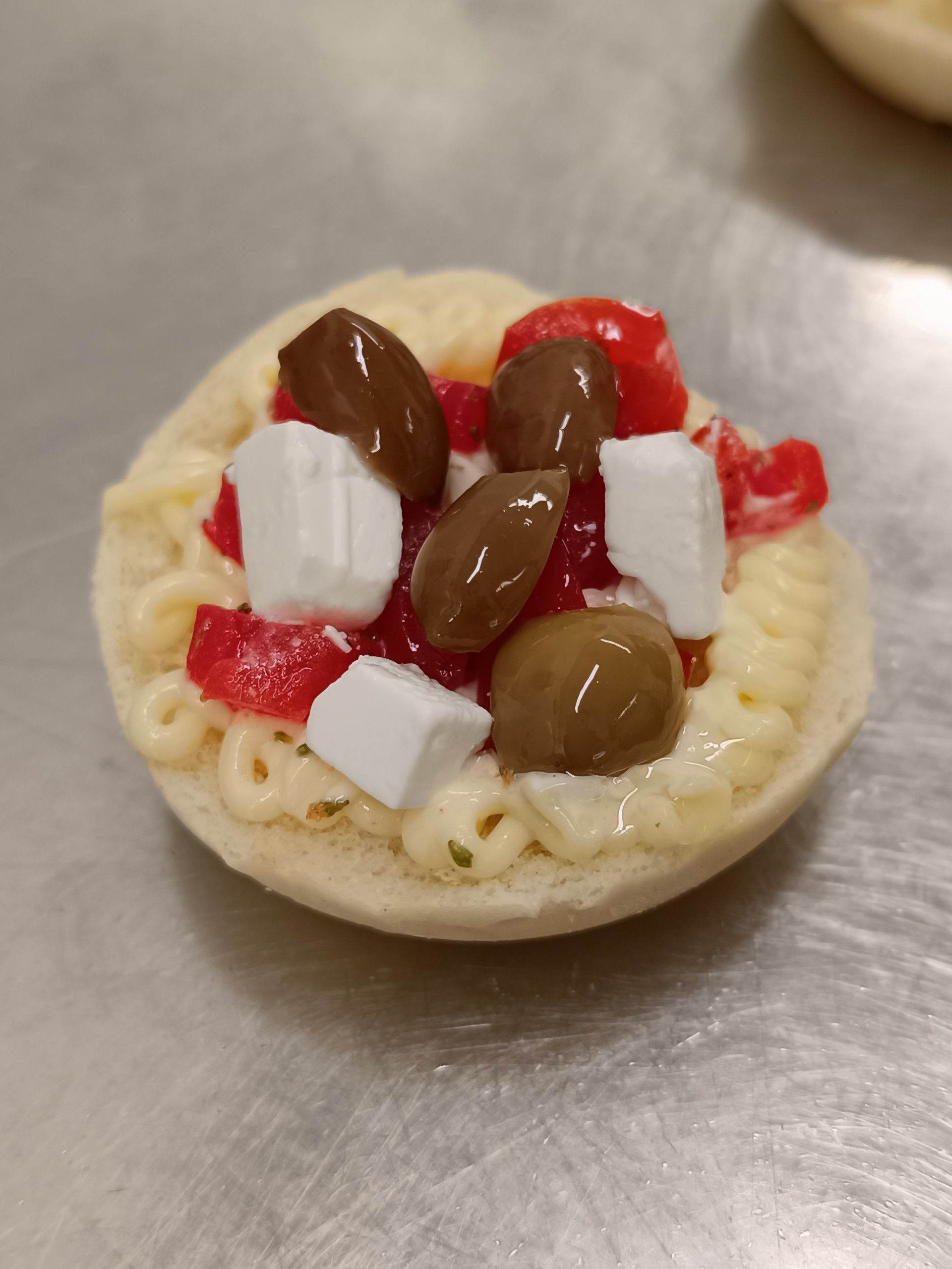 Una piccola pita aperta condita con formaggio, olive e pomodori rossi.