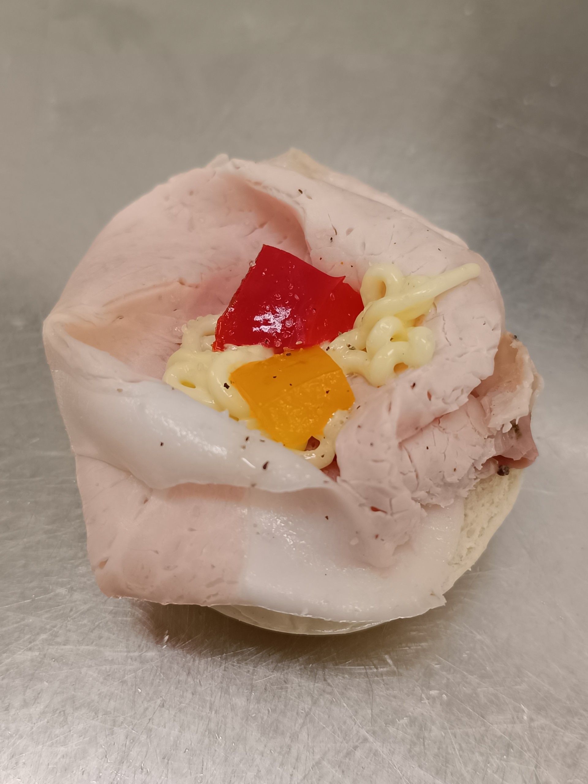 Involtino di prosciutto con peperoni rossi e arancioni e salsa su un panino.