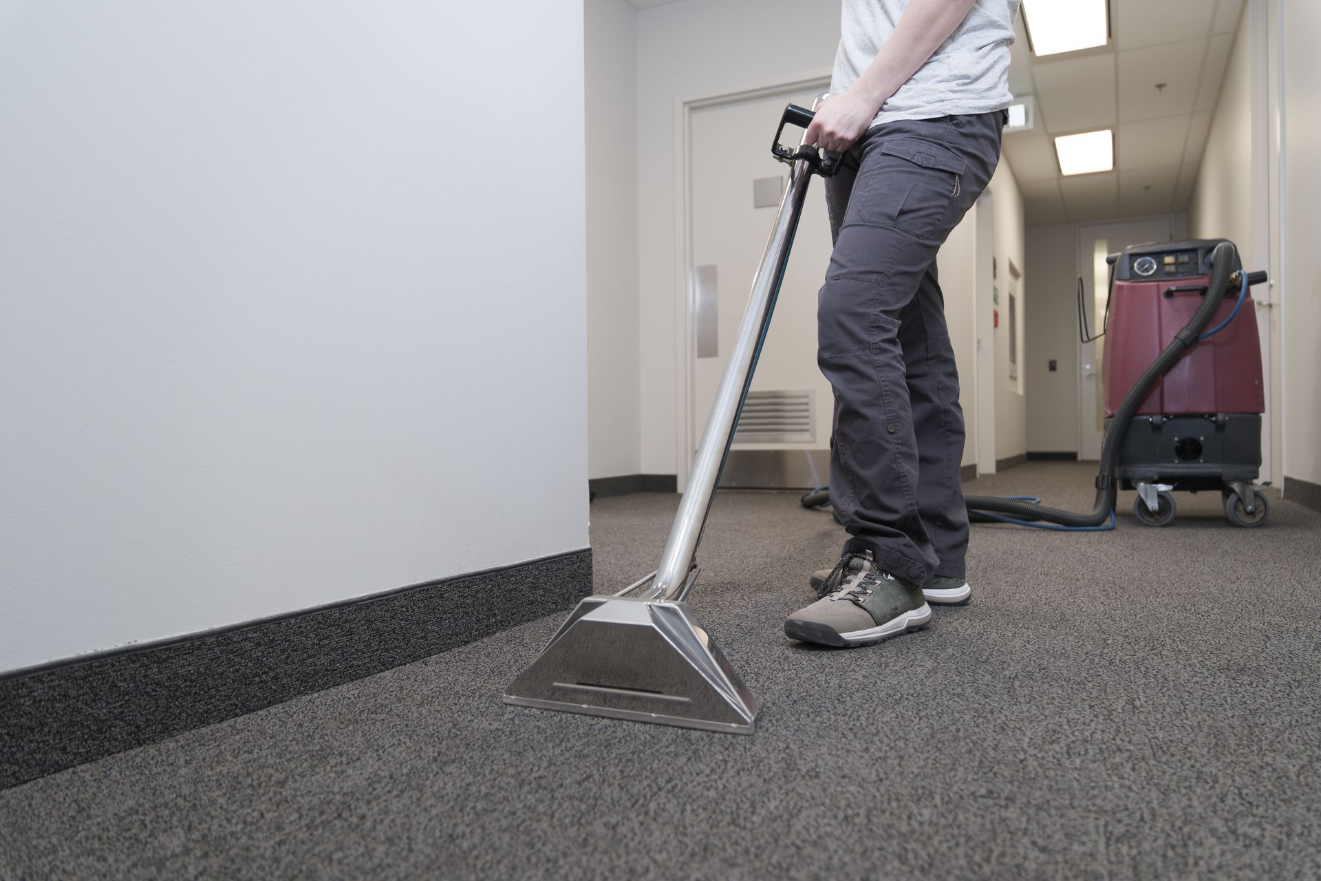 Person using a carpet cleaning machine in an office hallway