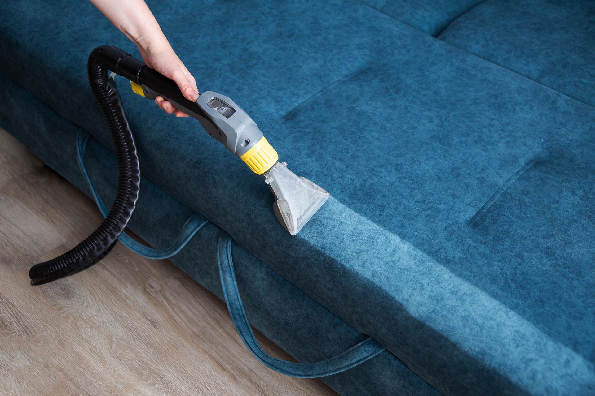 Person using a vacuum attachment to clean a blue upholstered couch