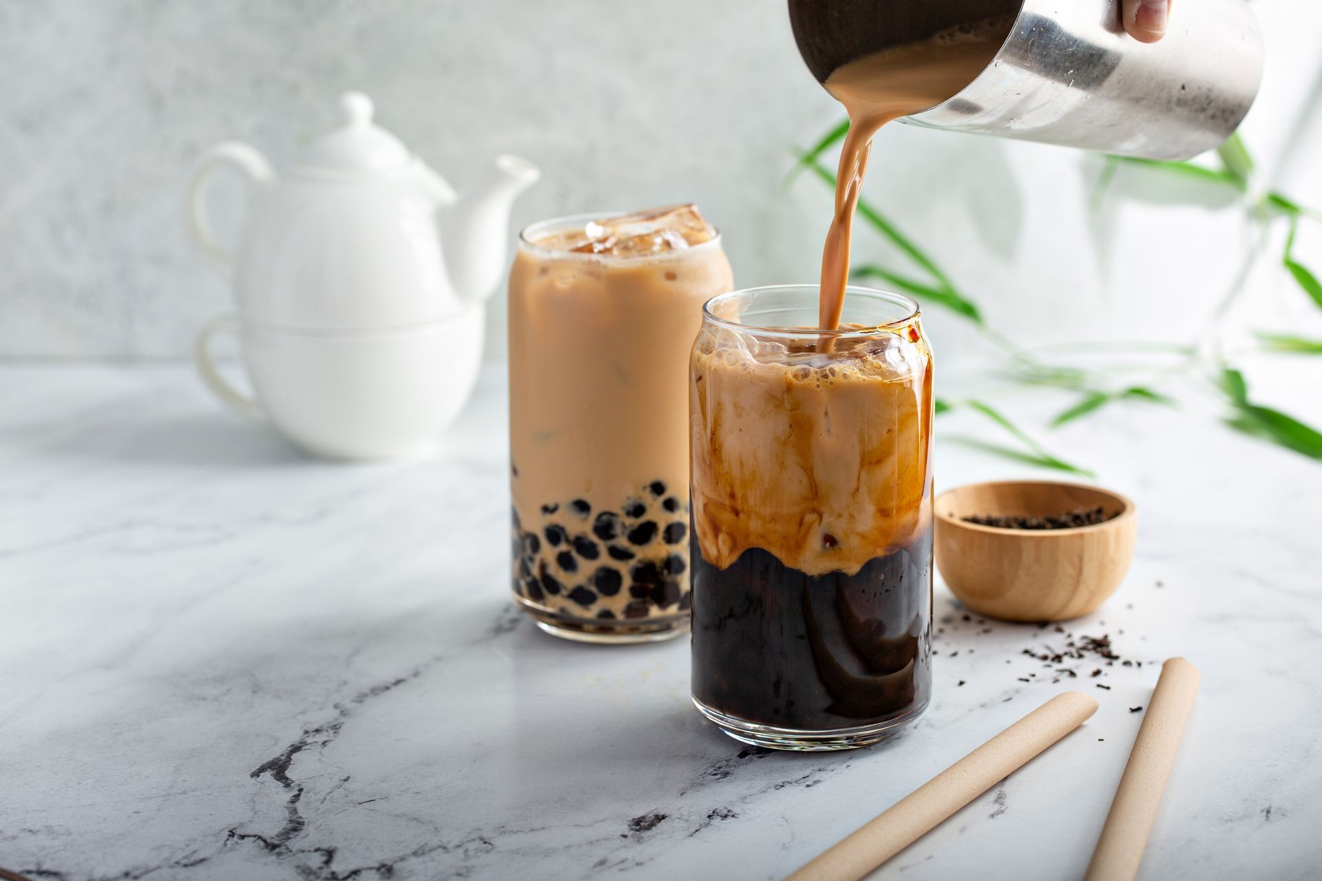 Boba milk tea in 2 tall glasses in a bright environment.
