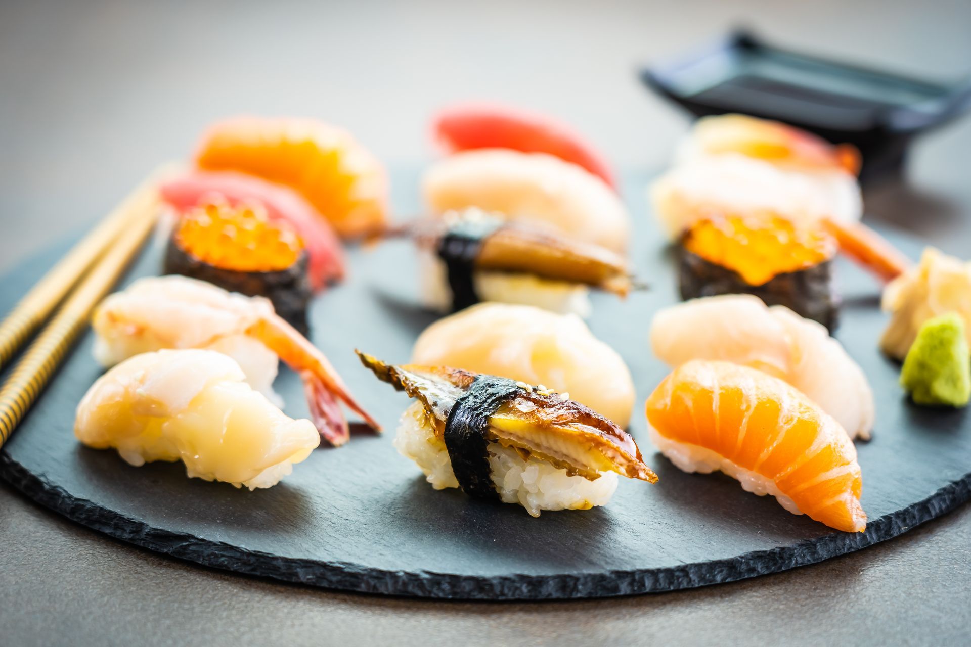 nigiri sushi set with salmon, tuna, shrimp, prawn, and eel on a black plate and chopsticks and sauce on side.