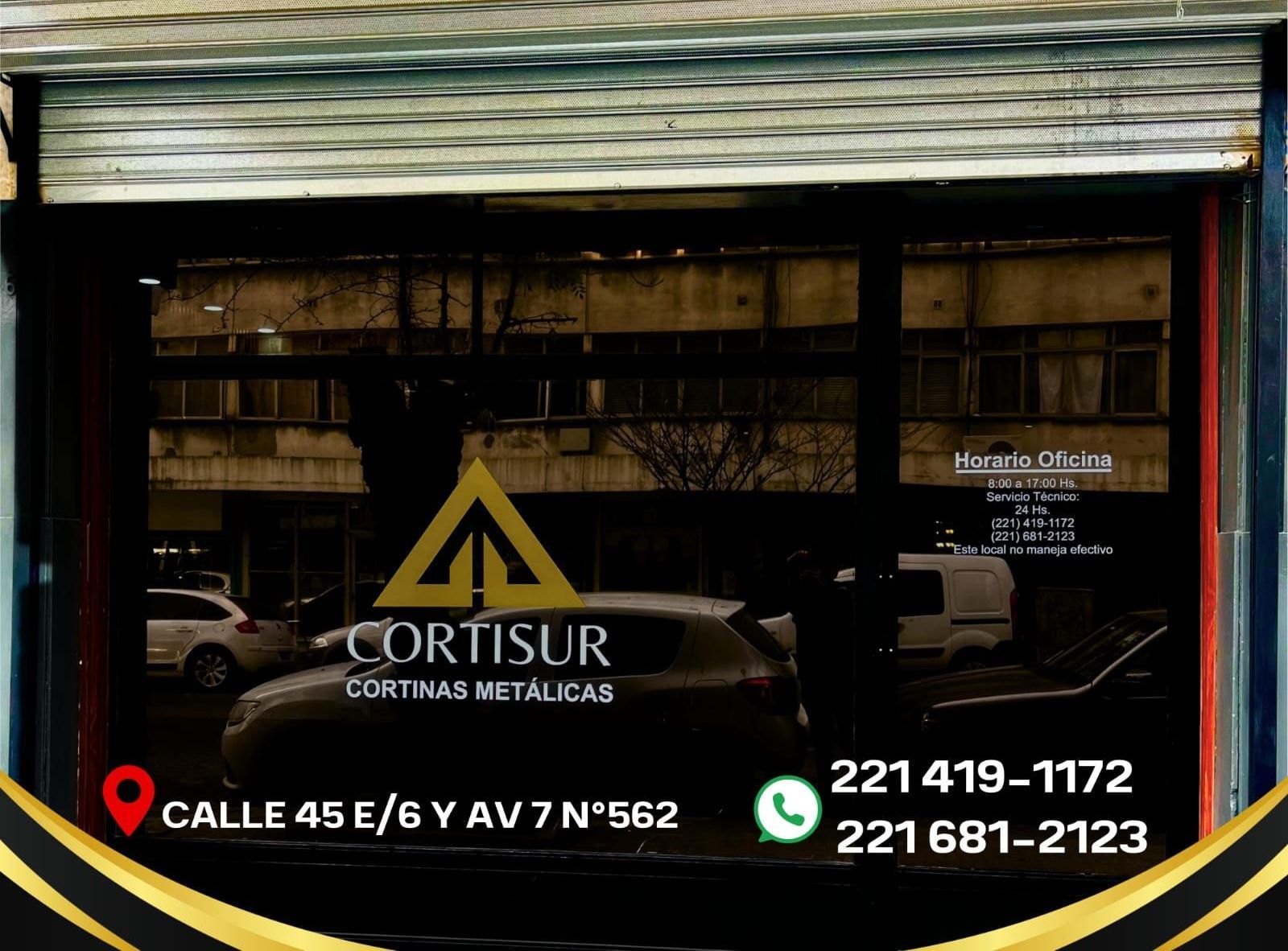 Cortinas metálicas Cortisur en el escaparate. Texto e información de contacto, dorado y negro. Vista de la calle, coche.