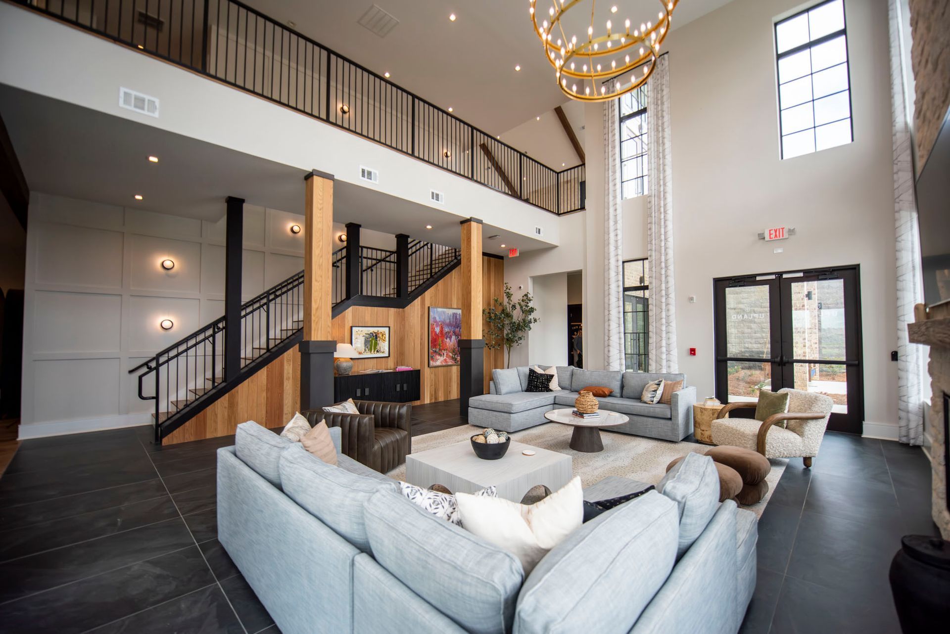 Spacious lobby with gray sectional sofas, staircase, and chandelier. Natural light streams in through large windows at Upland at Emerson in Emerson, GA.