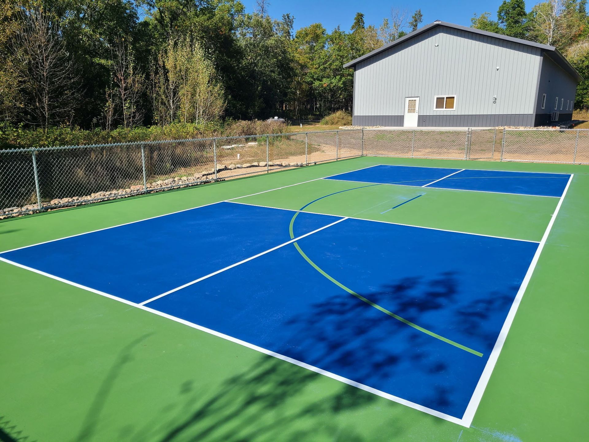 Blue and green outdoor court with a building in the background. Fenced perimeter.