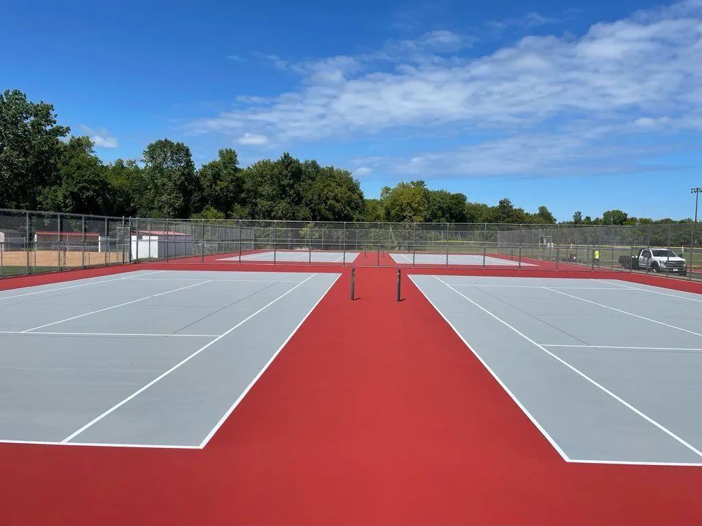 Empty outdoor tennis courts with a red walkway under a blue sky