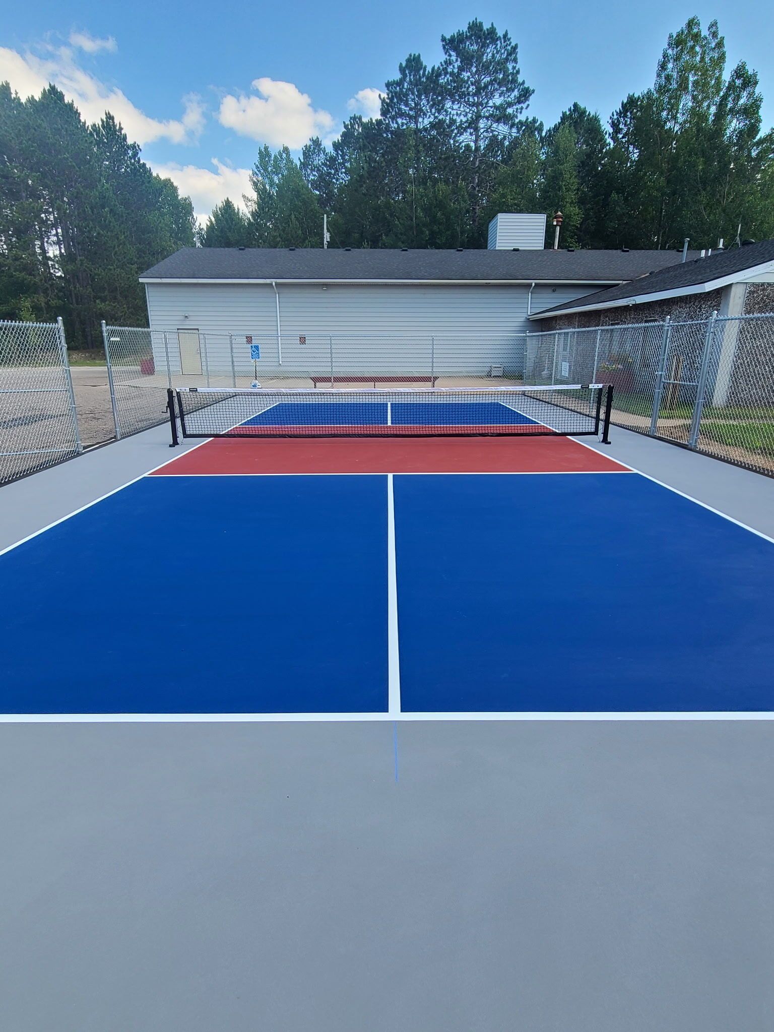 Pickleball court with a blue and red playing surface, nets, and a building in the background.